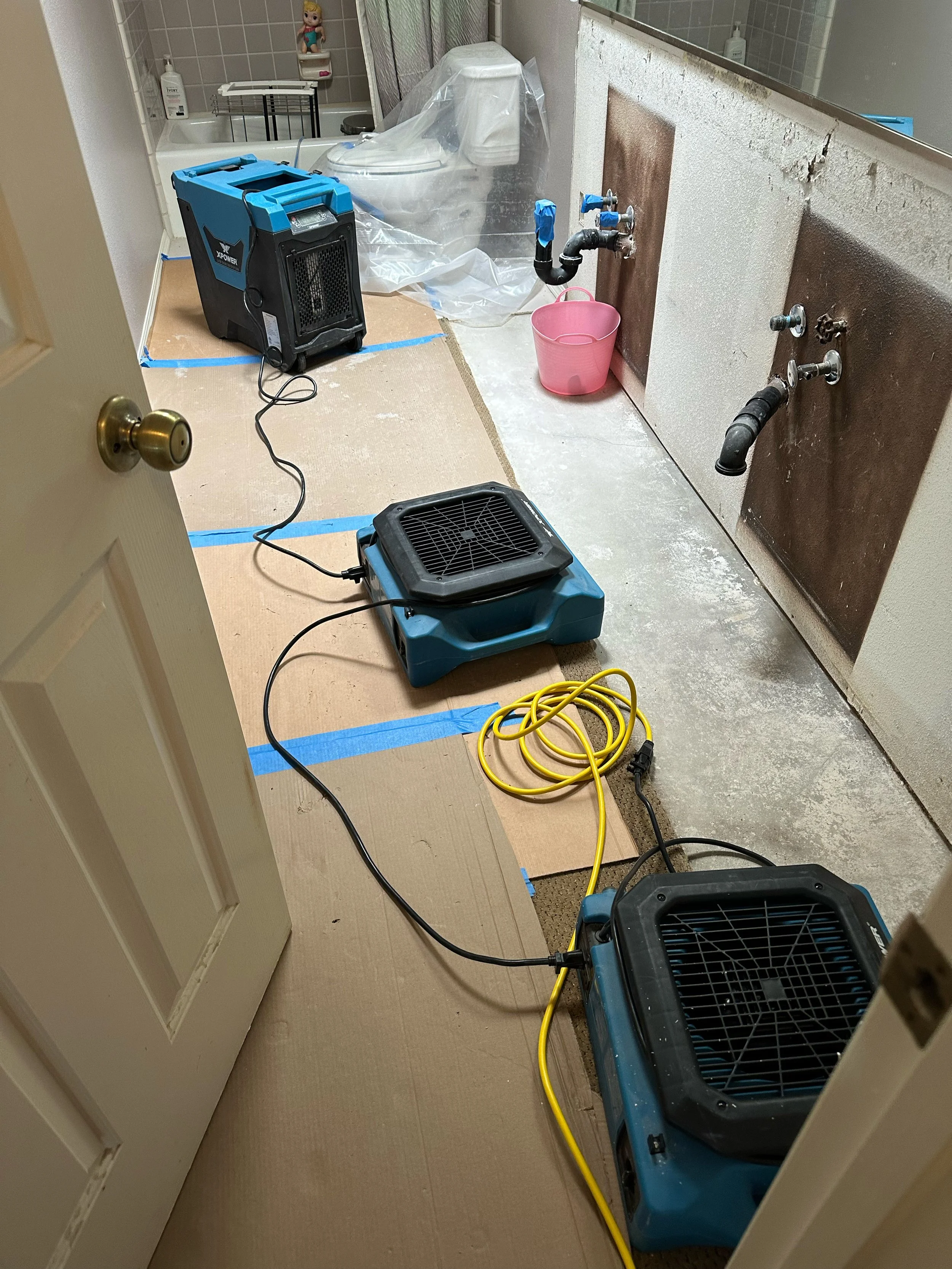 Water removal and drying equipment set up in an indoor bathroom.